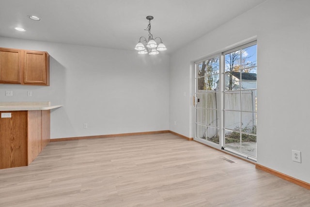 unfurnished dining area with light wood-type flooring, plenty of natural light, and a chandelier