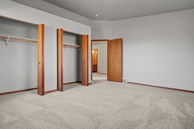 unfurnished bedroom with multiple closets and light carpet