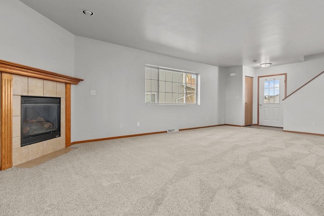 unfurnished living room with a tile fireplace, a healthy amount of sunlight, and light carpet