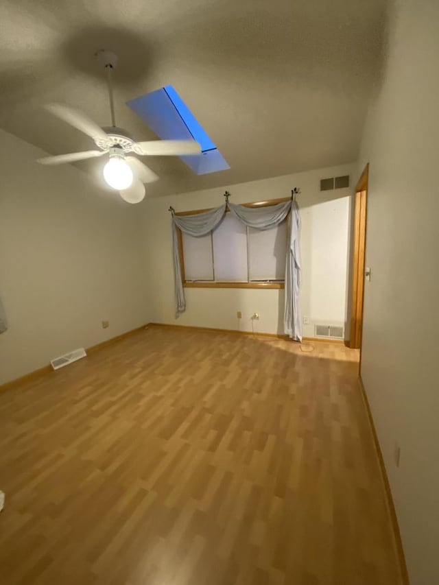 unfurnished room featuring a skylight, hardwood / wood-style flooring, and ceiling fan