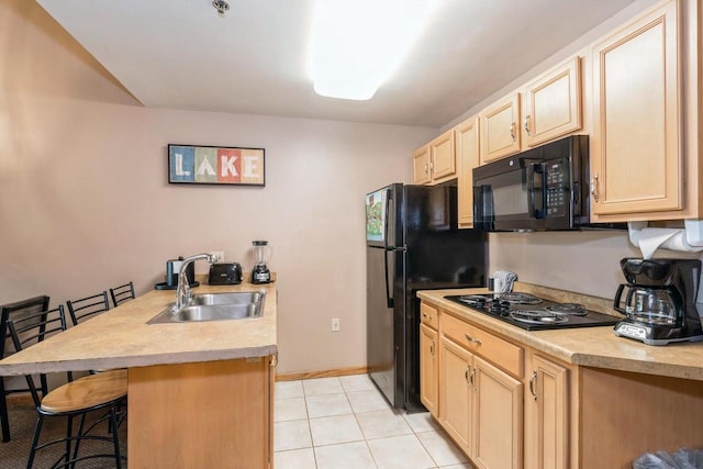 kitchen with light brown cabinetry, a breakfast bar, sink, and black appliances