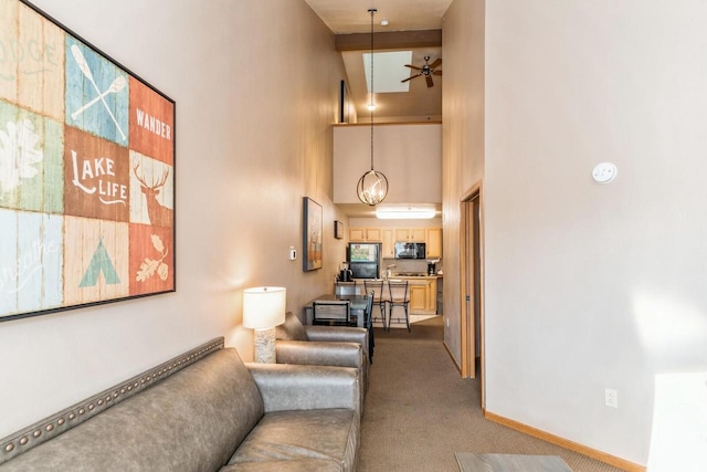 living room featuring beamed ceiling, carpet flooring, ceiling fan, and a towering ceiling