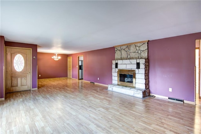 unfurnished living room with light hardwood / wood-style floors, a stone fireplace, and an inviting chandelier