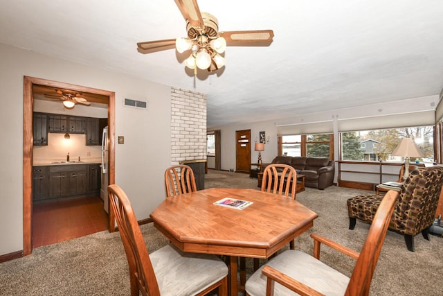 carpeted dining area with a fireplace, ceiling fan, and sink