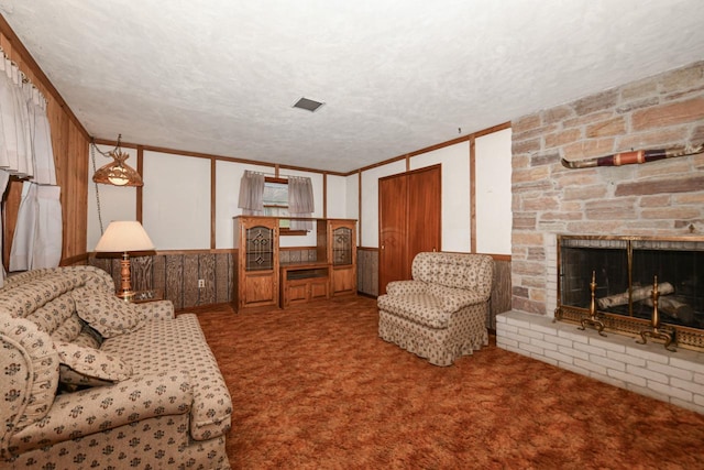 living room with a stone fireplace, carpet, a textured ceiling, and crown molding