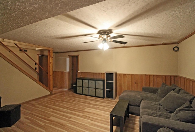 living room with light wood-type flooring, wooden walls, a textured ceiling, and ceiling fan