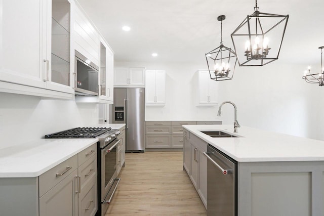 kitchen featuring gray cabinetry, a center island with sink, sink, hanging light fixtures, and stainless steel appliances