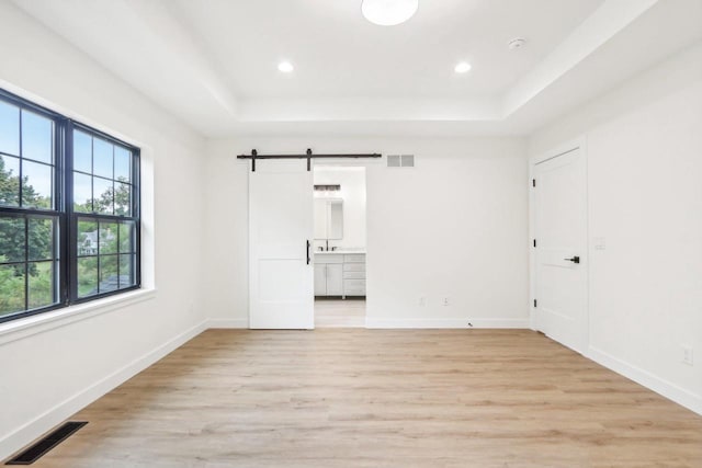 unfurnished bedroom featuring light wood-type flooring, a barn door, and a raised ceiling