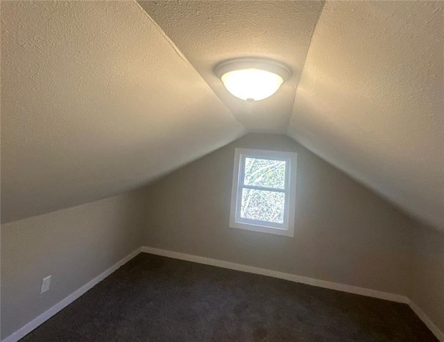 additional living space featuring a textured ceiling, vaulted ceiling, and dark carpet