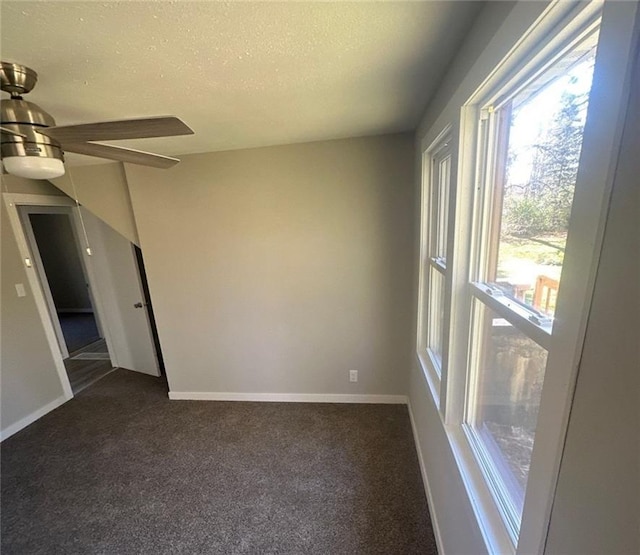 empty room with ceiling fan, plenty of natural light, a textured ceiling, and dark carpet