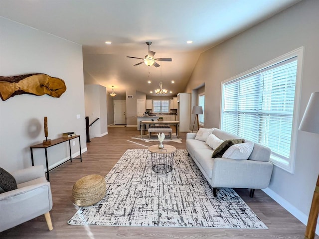 living room with wood-type flooring, ceiling fan with notable chandelier, and vaulted ceiling