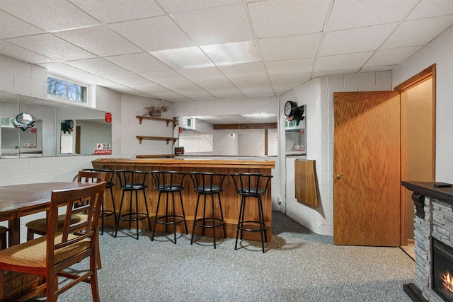 bar with a stone fireplace, a paneled ceiling, and carpet flooring