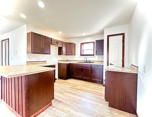 kitchen with dark brown cabinetry, sink, light wood-type flooring, and kitchen peninsula