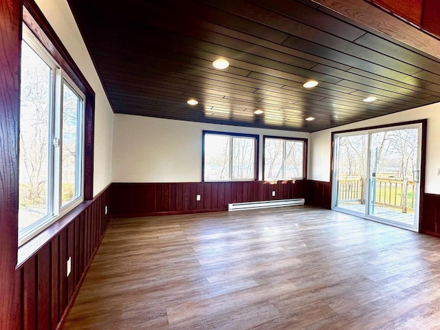 unfurnished room featuring wooden ceiling, baseboard heating, wooden walls, and light hardwood / wood-style flooring