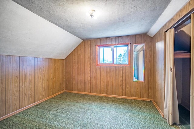 bonus room featuring carpet flooring, wood walls, a textured ceiling, and vaulted ceiling