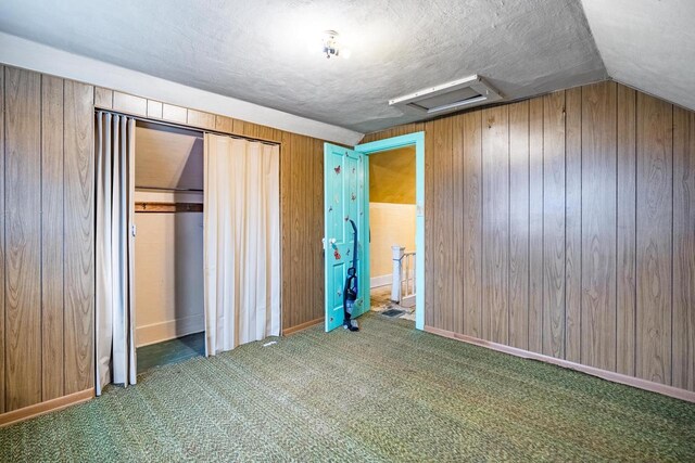 unfurnished bedroom featuring wooden walls, dark carpet, a closet, and lofted ceiling