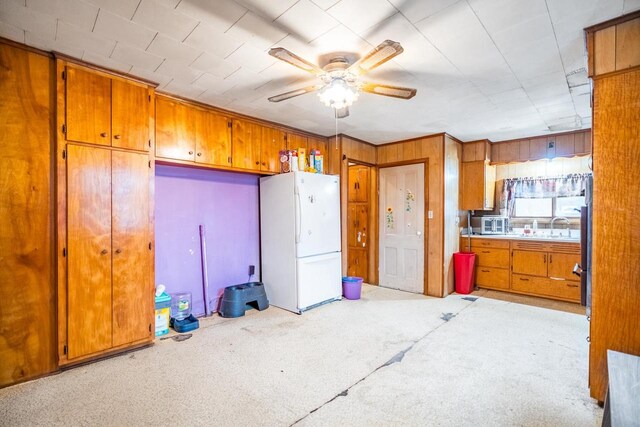 kitchen featuring ceiling fan, sink, light carpet, white refrigerator, and wooden walls