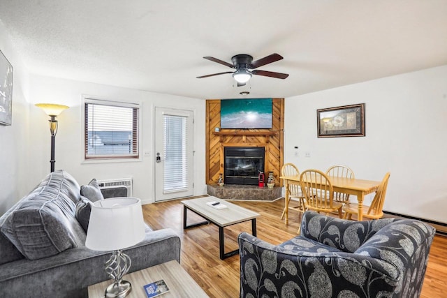 living room with a fireplace, light hardwood / wood-style floors, ceiling fan, and a baseboard radiator