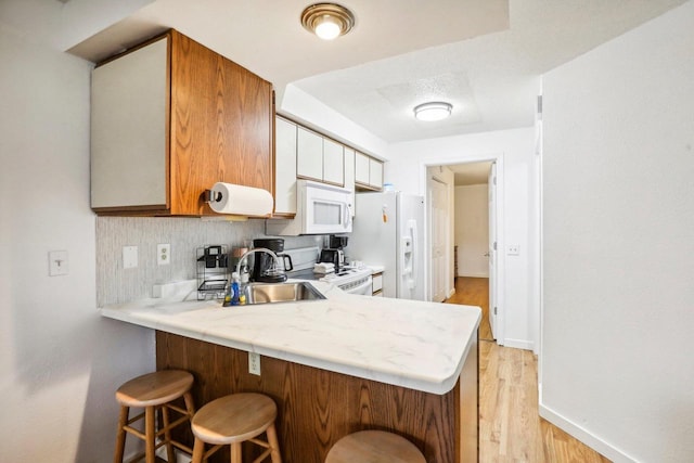 kitchen featuring light hardwood / wood-style floors, kitchen peninsula, sink, white cabinetry, and white appliances