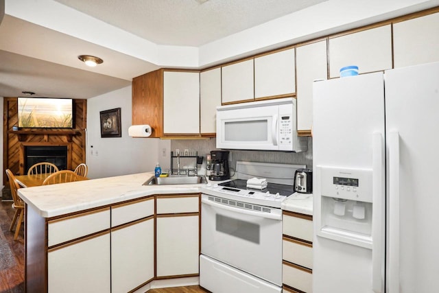 kitchen featuring white cabinetry, white appliances, hardwood / wood-style floors, a large fireplace, and kitchen peninsula