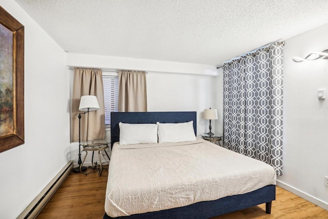 bedroom with a baseboard heating unit, hardwood / wood-style floors, and a textured ceiling