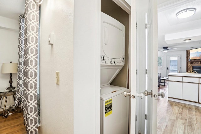 clothes washing area with light hardwood / wood-style floors, ceiling fan, and stacked washer / dryer