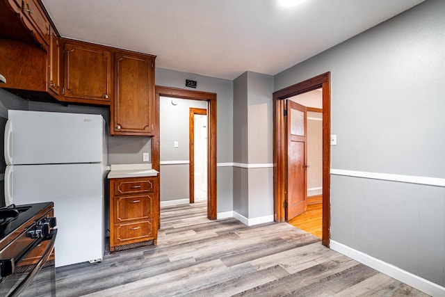 kitchen featuring black electric range oven, light hardwood / wood-style floors, and white fridge