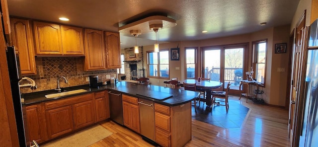 kitchen with light wood-type flooring, decorative light fixtures, sink, stainless steel dishwasher, and kitchen peninsula