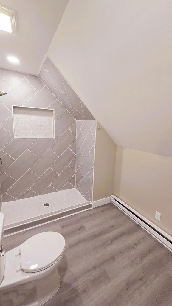 bathroom featuring a tile shower, baseboard heating, hardwood / wood-style flooring, toilet, and lofted ceiling