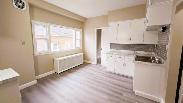 kitchen featuring radiator, sink, decorative backsplash, light hardwood / wood-style floors, and white cabinetry