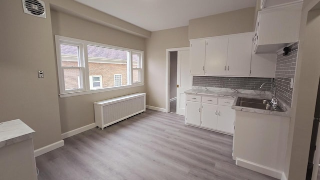 kitchen with tasteful backsplash, radiator, sink, light hardwood / wood-style flooring, and white cabinets