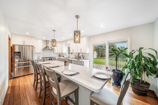 kitchen featuring wall chimney range hood, white cabinetry, pendant lighting, and appliances with stainless steel finishes