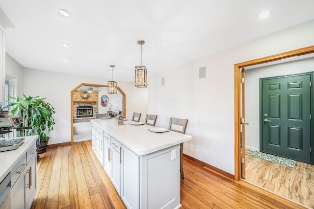 kitchen with a kitchen breakfast bar, a kitchen island, pendant lighting, light hardwood / wood-style flooring, and white cabinetry