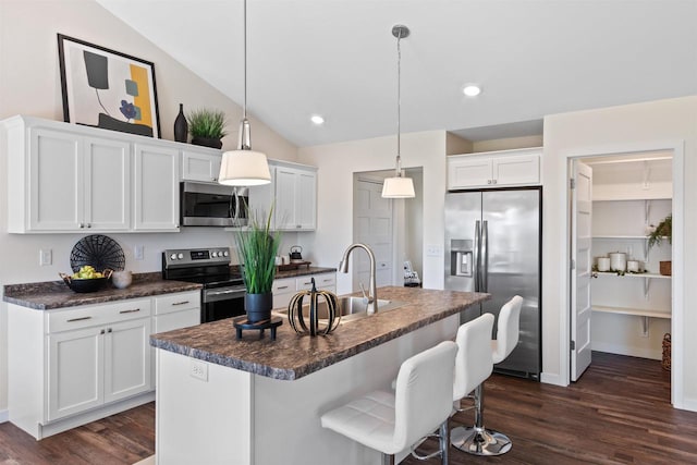 kitchen with a center island with sink, appliances with stainless steel finishes, hanging light fixtures, lofted ceiling, and white cabinets