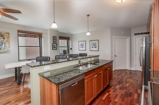 kitchen with sink, hanging light fixtures, stainless steel appliances, dark hardwood / wood-style flooring, and a center island with sink