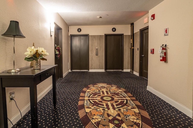 corridor featuring elevator, dark carpet, and a textured ceiling