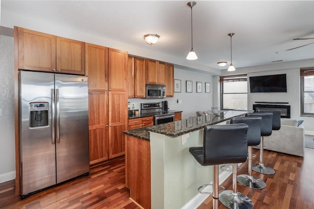 kitchen featuring a kitchen bar, stainless steel appliances, dark hardwood / wood-style floors, and dark stone countertops