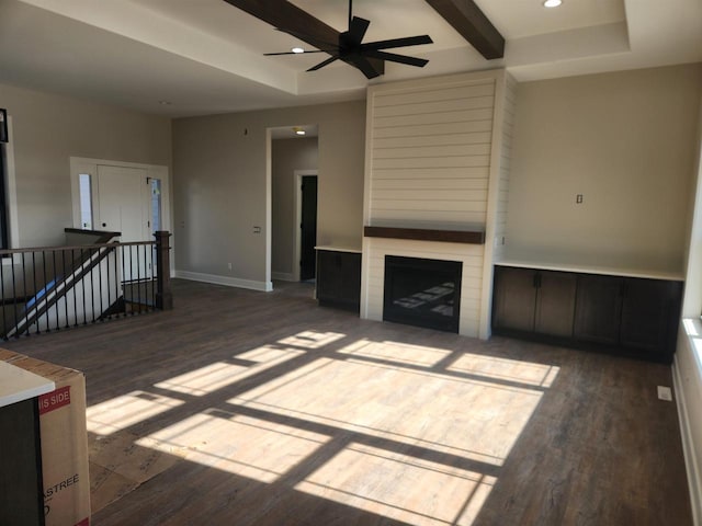 unfurnished living room featuring dark hardwood / wood-style flooring, ceiling fan, a fireplace, and beamed ceiling