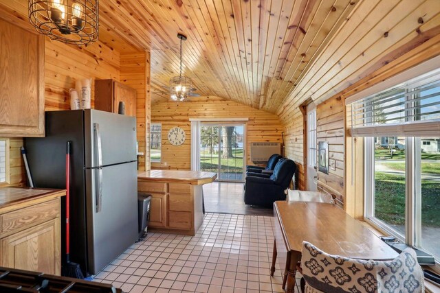 kitchen featuring vaulted ceiling, wood walls, stainless steel refrigerator, light brown cabinets, and decorative light fixtures