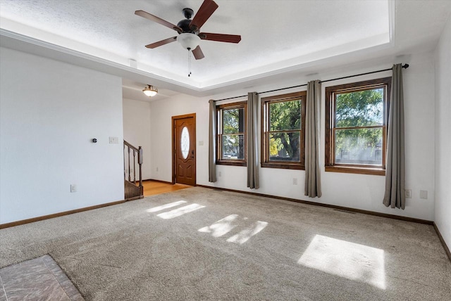 interior space with a wealth of natural light, light colored carpet, ceiling fan, and a raised ceiling