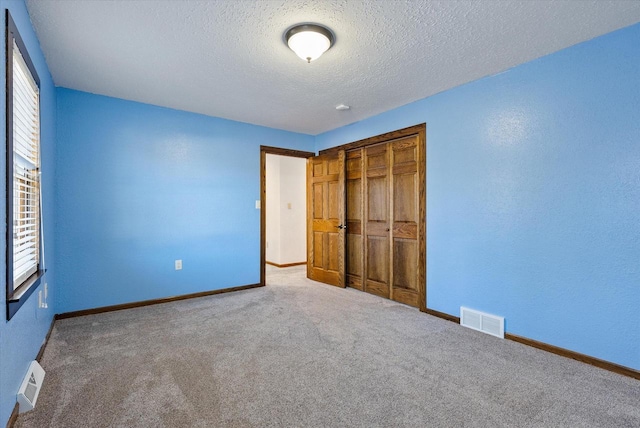 unfurnished bedroom with a closet, multiple windows, a textured ceiling, and carpet flooring