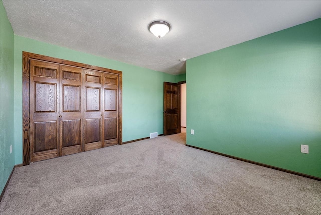 unfurnished bedroom featuring a textured ceiling, light carpet, and a closet