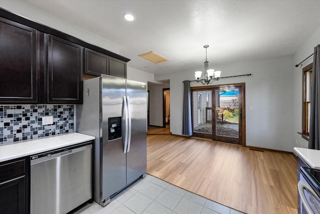 kitchen featuring stainless steel appliances, pendant lighting, an inviting chandelier, decorative backsplash, and light hardwood / wood-style flooring