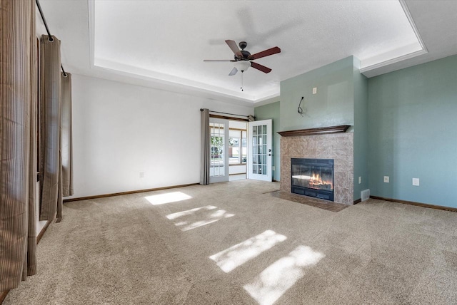 unfurnished living room with a tray ceiling, french doors, carpet flooring, and ceiling fan