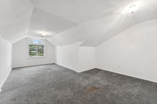 bonus room with a textured ceiling, vaulted ceiling, and dark carpet