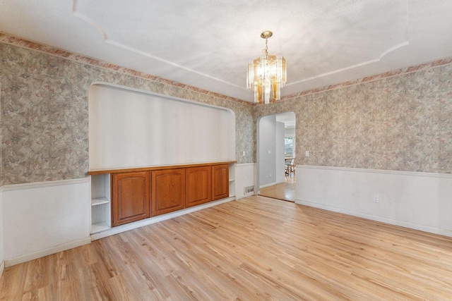 unfurnished dining area with light hardwood / wood-style floors, a chandelier, and a textured ceiling