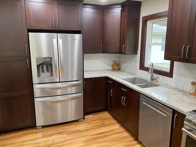 kitchen with tasteful backsplash, light stone counters, appliances with stainless steel finishes, sink, and light hardwood / wood-style floors