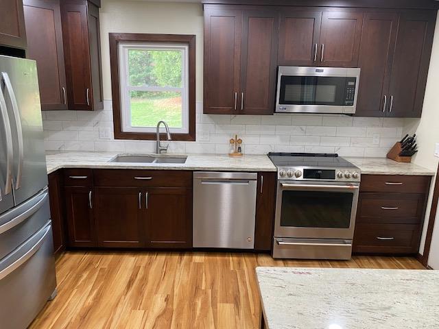 kitchen with stainless steel appliances, decorative backsplash, sink, light stone countertops, and light hardwood / wood-style flooring