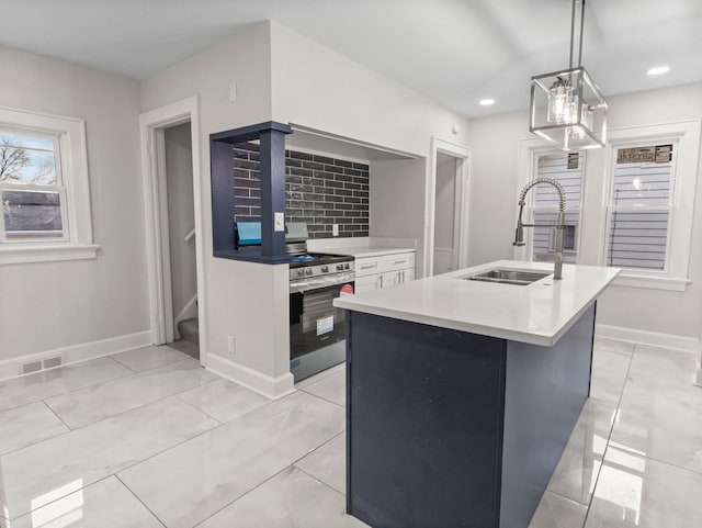 kitchen featuring sink, hanging light fixtures, an island with sink, decorative backsplash, and stainless steel stove