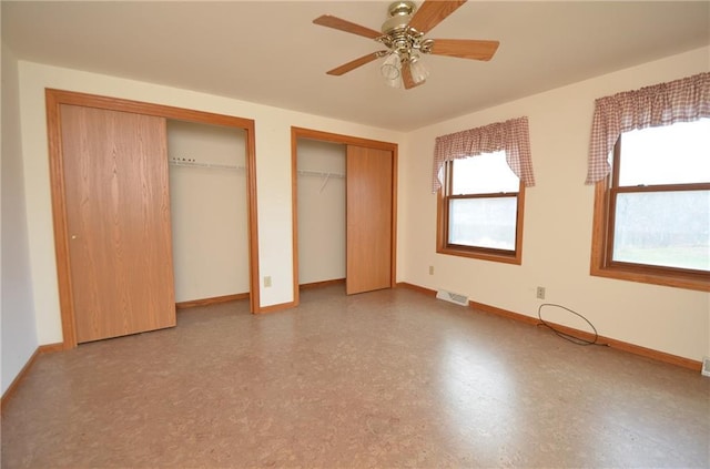 unfurnished bedroom with ceiling fan, multiple windows, and multiple closets